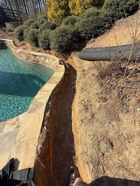 French drain trench cut alongside a pool deck
