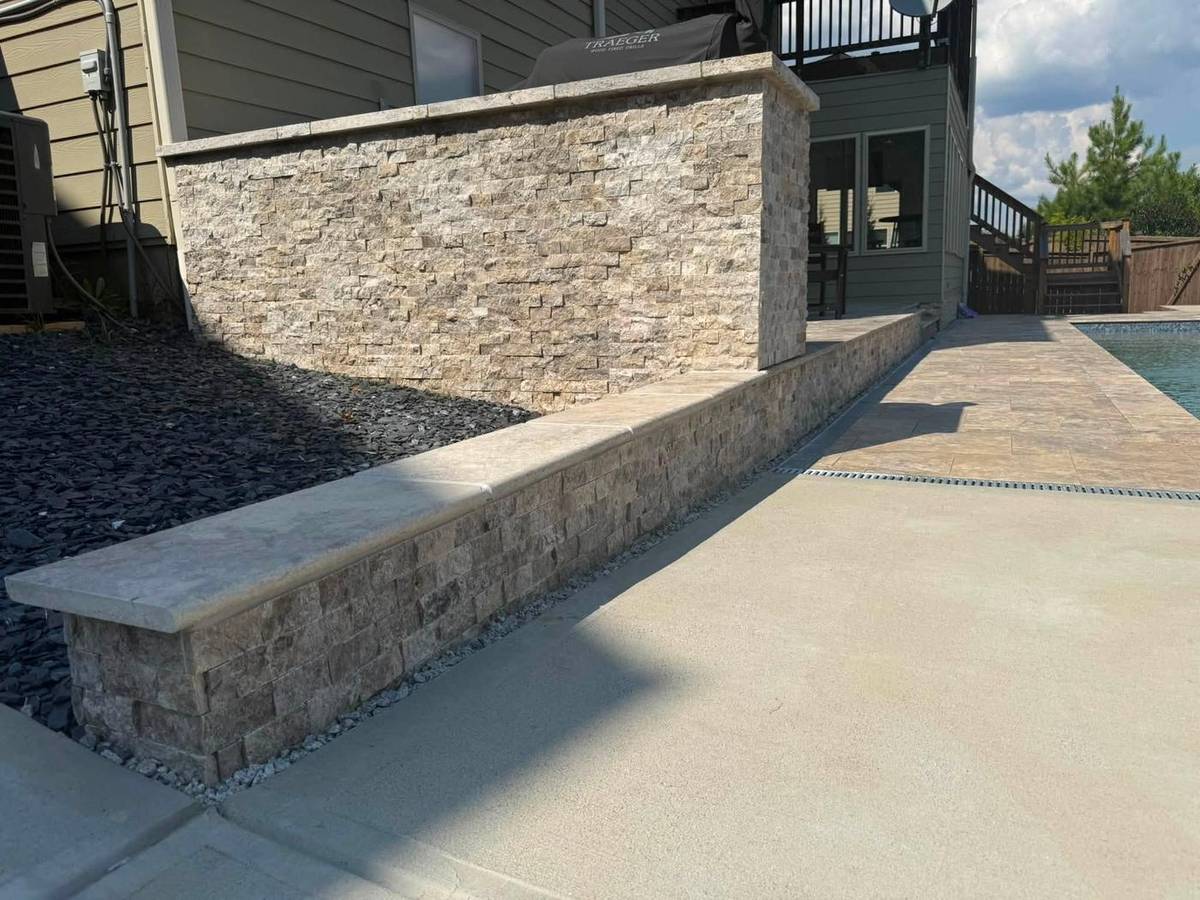 Stacked stone seat wall alongside a poured concrete patio and walkway